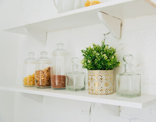 Kitchen interior. A shelf with a vase of flowers and glass jars of cereals and pasta.