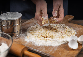 Women's hands, flour and dough. A woman in an apron prepares dough for homemade baking, a rustic home cozy atmosphere, a dark background with unusual lighting.