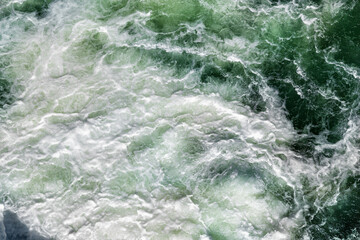 Fototapeta na wymiar Close-up abstract texture above view of river torrent and clear fresh cold water flowing through mountain rocks in valley with foam and bubbles on sunny day. Nature force and power background