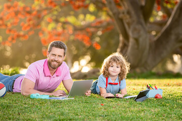Naklejka na ściany i meble Son with father learning outdoor by studying online and working on laptop in green field.