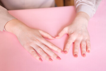 
Female hands on a pink background. Beautiful well-groomed hands with classic manicure. The fingers show the heart.