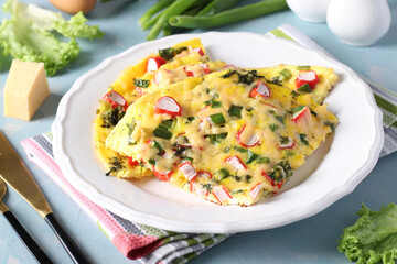 Omelet with crab sticks, cheese and green onions on a white plate on a light blue background. Closeup. © Anzhela
