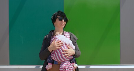 Woman posing, she uses a sling on the body. Securing the child nearby, natural parenting. Calmness of the kid on a walk. Green background.