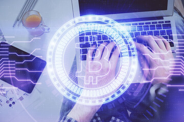 Double exposure of man's hands typing over computer keyboard and crypto currency theme hologram...