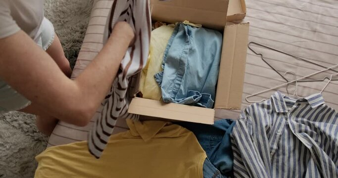 Woman packing used casual clothes into box to sell online as second hand or donation, sustainable living concept.