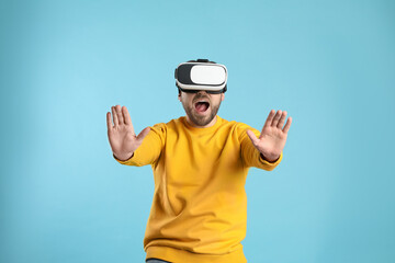 Fototapeta premium Emotional man using virtual reality headset on light blue background