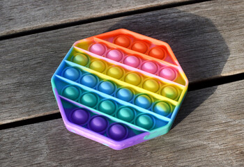 Trendy silicone colorful rainbow antistress pop it toy for baby on wooden background. Top view.