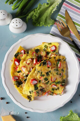 Omelet with crab sticks, cheese and green onions on a white plate on a light blue background. Top view