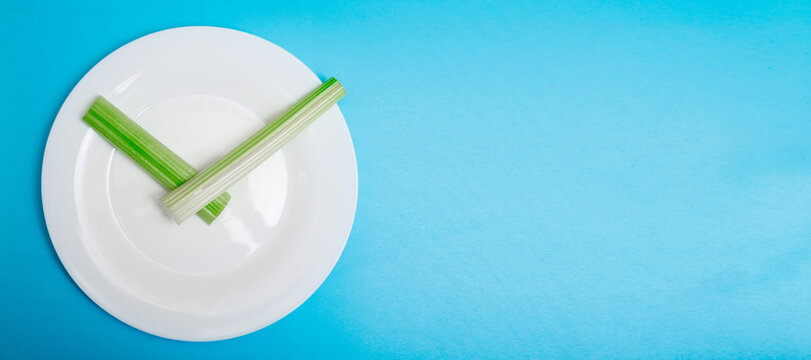 Intermittent fasting, diet concept. Banner. An empty plate as a dial and pods of a seler as a clock hands on a blue background.