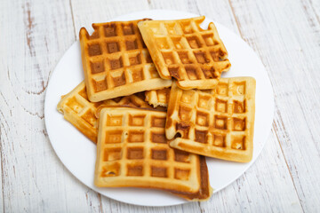 Freshly cooked Belgian waffles on a white plate on a light wooden background.