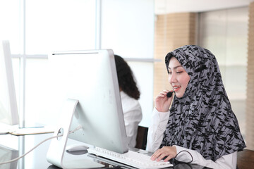 Asian Muslim female  with headsets working in a call centre,Call center agent with headset working on support hotline in modern office. Call center worker accompanied by her team. speaking to partner