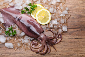 Fresh raw squid with ice, lemon and parsley on wooden table, flat lay