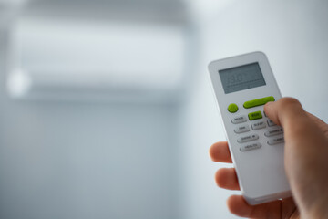 Close-up of male hand using remote control of split air conditioner.