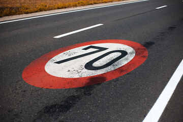Close-up view of 70 km per hour, speed limit sign painted on dark asphalting road.