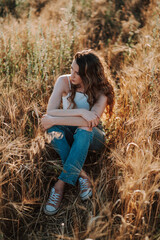 Chica joven atractiva posando en campo de trigo al atardecer con tonos dorados