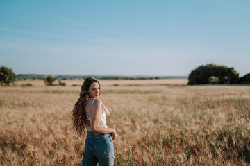 Chica joven atractiva posando en mitad de un campo de trigo al atardecer con tonos dorados