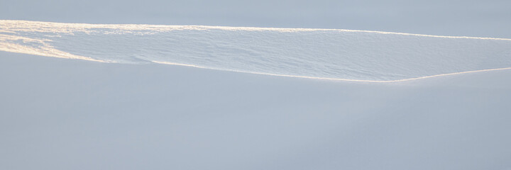 Beautiful winter background with snowy ground. Natural snow texture. Wind sculpted patterns on snow surface. Wide panoramic texture for background and design. Closeup top view with copy space.