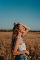 Chica joven atractiva posando en campo de trigo al atardecer con tonos dorados