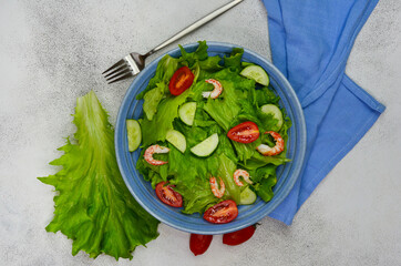 fresh summer salad of vegetables lettuce leaves, cherry tomatoes, cucumber slices and shrimp, seafood dish isolated on a white background