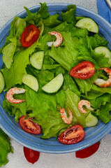 fresh summer salad of vegetables lettuce leaves, cherry tomatoes, cucumber slices and shrimp, seafood dish
