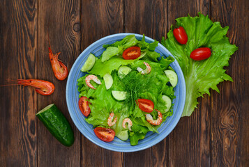 fresh summer salad of vegetables lettuce leaves, cherry tomatoes, cucumber slices and shrimp, seafood dish isolated on a white background