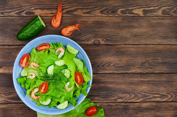 fresh summer salad of vegetables lettuce leaves, cherry tomatoes, cucumber slices and shrimp, seafood dish, copy space