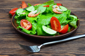 fresh summer salad of vegetables lettuce leaves, cherry tomatoes, cucumber slices and shrimp, seafood dish isolated on a white background