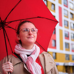 Women with a red umbrella in the rain on the background of a colored building