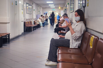 Pregnant woman with phone in clinic lobby with medical mask on face