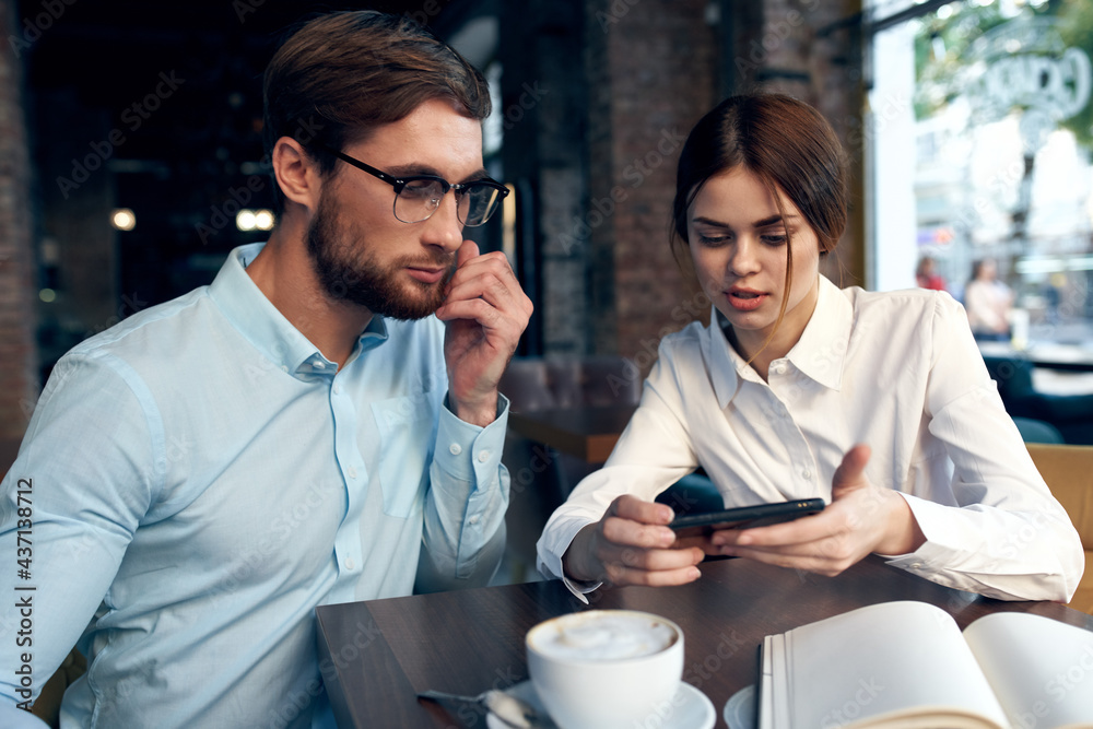 Wall mural business man and woman sitting at a table in a cafe and looking at the phone