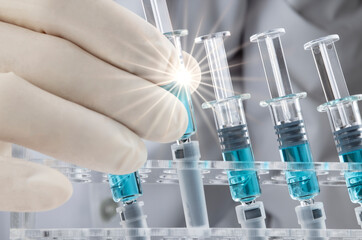 Closed up image of a doctor holding a glass syringe with several other syringes prefilled with blue...