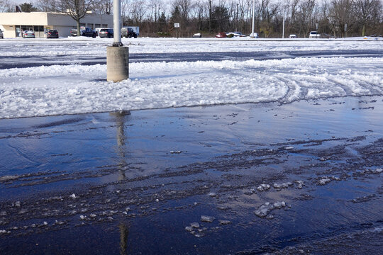 A partially plowed parking lot covered with ice, snow and slush on a sunny day
