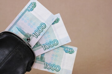 Retro black wallet and three banknotes with a face value of 1000 rubles sticking out of it.