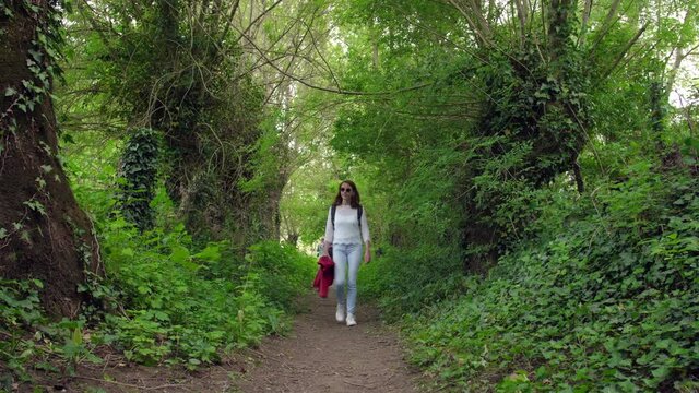 Young woman wearing neutral clothing walking along a woodland path on a sunny day - model released 4K May 2021