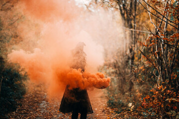 Girl dressed as witch in orange smoke on forest background