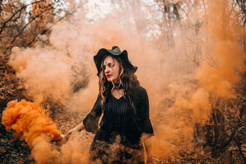 Girl dressed as witch holding smoke bomb in her hands on forest background