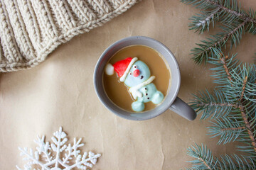 Composition of the new year, a gray mug with coffee marshmallows in the form of a snowman in a red hat.