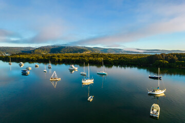 Early morning aerial waterscape with boats, light cloud and fog
