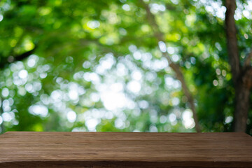 Abstract bokeh sunlight and tree background of nature in green color with wood table.	
