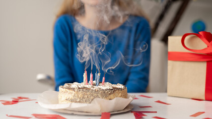 The cake on the table with extinguished candles is smoking and a girl is silhouetted in the...