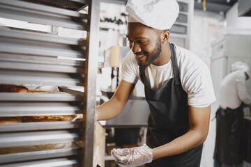 African American baker in uniform sorting baked products on pallets