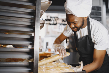 African American baker in uniform sorting baked products on pallets
