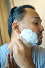 Asian man hand implies of shaving beard with razor.