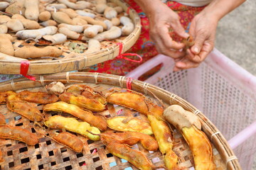 Old Asian woman crack ripe sour tamarind peel for make soggy tamarind, close up ripe sour tamarind on wooden basket