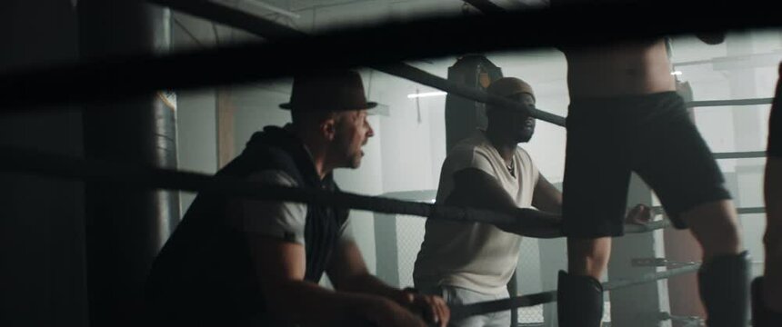 HANDHELD Coaches standing near boxing ring, cheering their fighters during kickboxing match sparring. Shot with 2x anamorphic lens