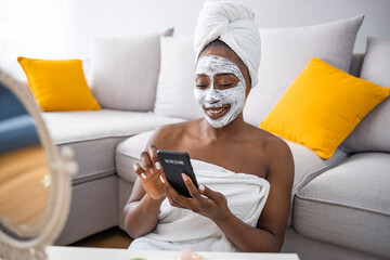 Young woman using mobile smartphone while having skin care spa day at home. Beautiful woman applying facial mask and using mobil phone. Lifestyle.