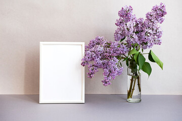 Mock up photo frame in minimalistic interior. Modern still life scene of white frame and bouquet of lilacs. Concept trendy home decor. Banner in pastel colors.