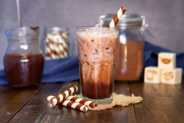 Iced cocoa, cocoa powder, chocolate wafer sticks on a wooden table