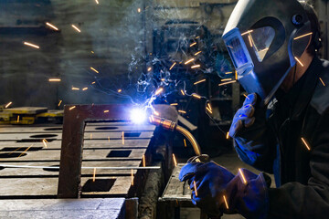 An electric and gas welder in an electromechanical workshop welds a metal structure at a mechanical...