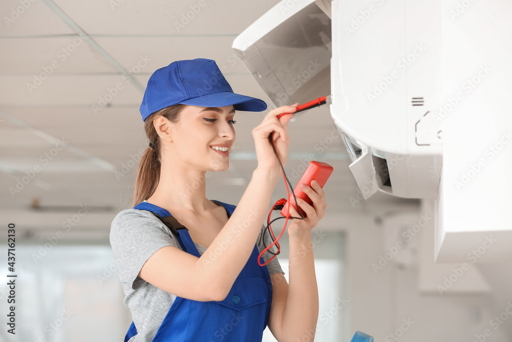 Wall mural young female electrician measuring voltage of air conditioner in room